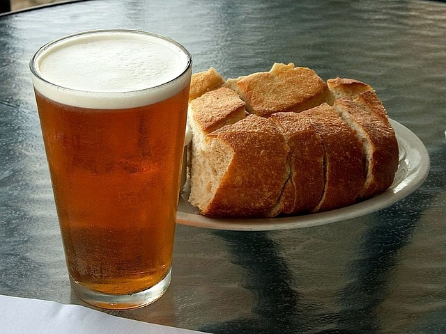 Ein Glas Bier steht neben einer Platte mit frisch geschnittenem Brot.