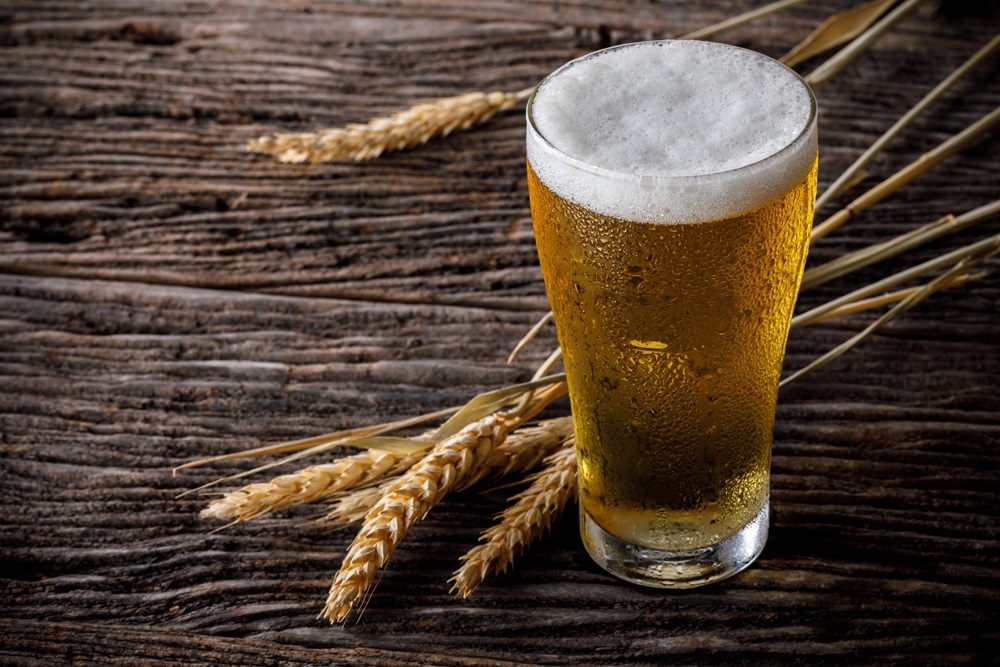 Kühles Glas Bier mit Schaumkrone auf rustikalem Holztisch, dekoriert mit Gerstenähren.