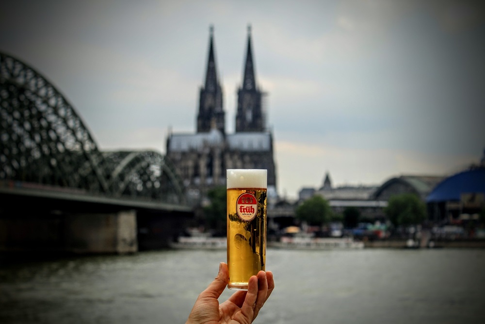 Ein Glas Kölsch, das vor dem Kölner Dom gehalten wird.