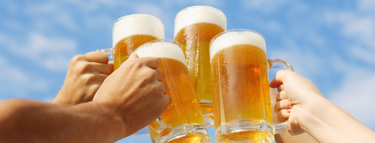 Vier Menschen stoßen unter blauem Sommerhimmel mit Leichtbier an.